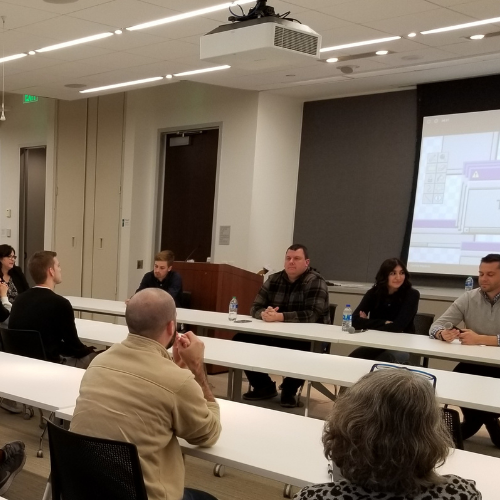 Table with panelists in front of room and tables with male and female adults listening
