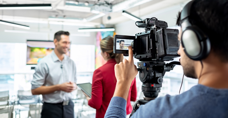 Videographer shooting businessman during corporate interview with female journalist.