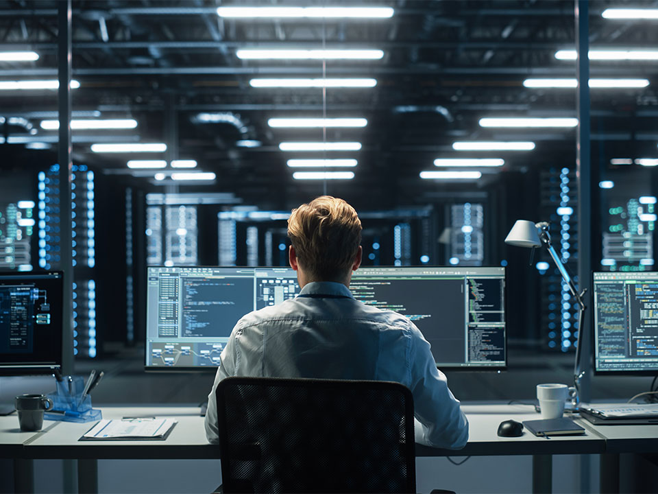 Man sitting in front of multiple computer monitors in a system control room of a data center