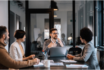 Group of employees sitting around conference table talking