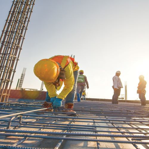 Man in hardhat and safety vest kneeling and working on an industrial construction project