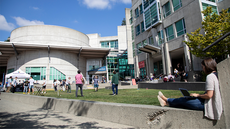 Students enjoying various outdoor activities such as studying, frisbee, and spirit activities on the Quad at Capilano University.